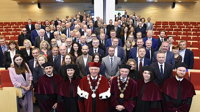 grupa ludzi ubranych formalnie stoi obok siebie w sali
