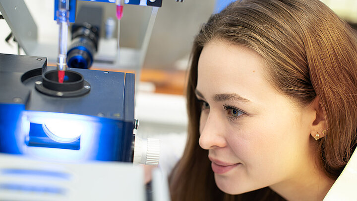 Zbliżenie na twarz kobiety spoglądającej na aparaturę badawczą automatycznie dozującą płyn.