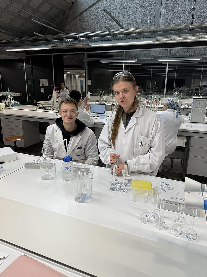 dwóch młodych mężczyzn ubranych w fartuchy znajduje się w laboratorium