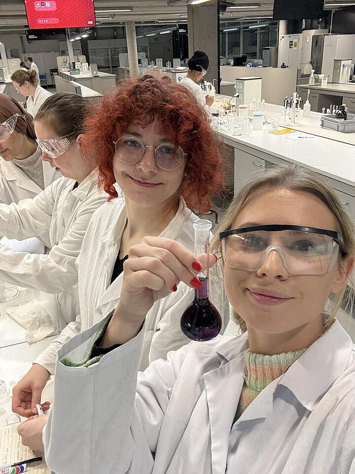 dwie młode kobiety ubrane w fartuchy laboratoryjne uśmiechają się do zdjęcia