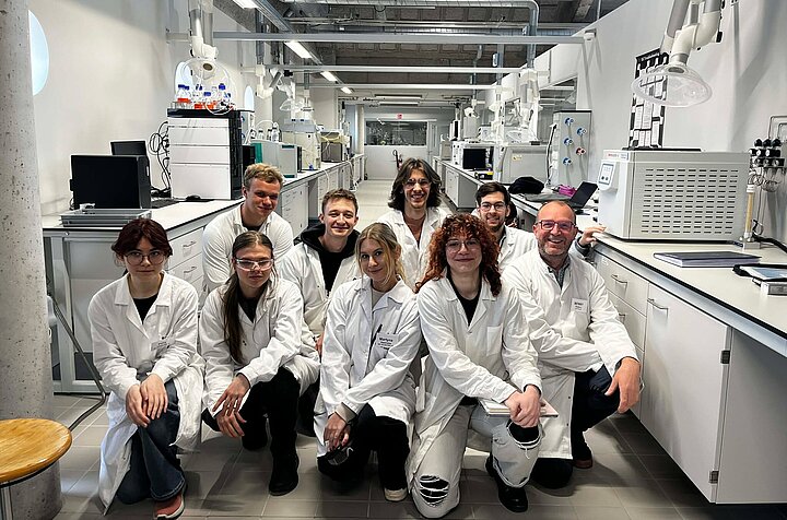 gruapa młodych ludzi ubranych w fartuchy laboratoryjne kuca w laboratorium